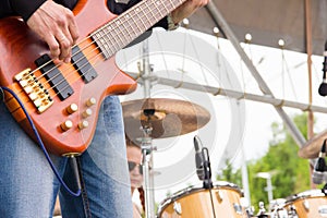 Musical band perfom on an open air festival. Bass guitarist man playing close, drums blurry