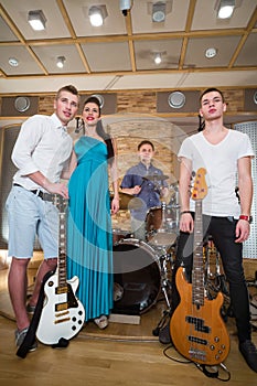 Musical group of three guys and one girl are standing