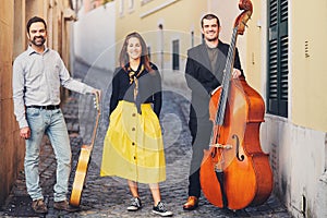 A musical group of three people on an old European street. The band consists of two men and one girl. Men with a double bass and a