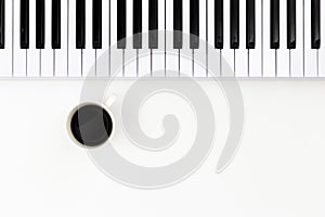 Musical keyboard and a cup of coffee on a white background, top view.