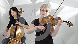 Musical quartet girls performs the composition on three violins and cello. White studio