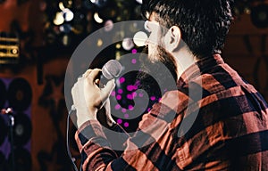 Musician with beard singing song in karaoke, rear view. Man in checkered shirt holds microphone, singing song, karaoke