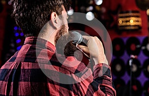 Musician with beard singing song in karaoke, rear view. Rock singer concept. Guy likes to sing in dark karaoke hall. Man