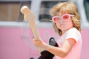 Musician child with a guitar. Joyful cute kid improvising. Happy kid enjoys music over colorful pink background.