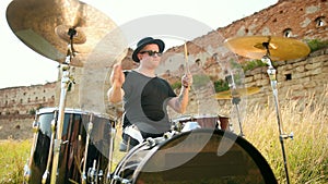 Musician drummer dressed in black clothes, hat, playing the drum set and cymbals