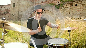 Musician drummer dressed in black hat, playing drum set and cymbals, on street