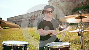 Musician drummer dressed in black hat, playing drum set and cymbals, on street