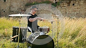 Musician drummer dressed in black hat, playing drum set and cymbals, on street