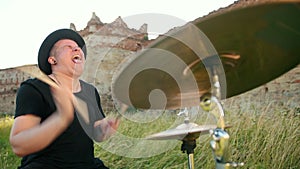 Musician drummer dressed in black hat, playing drum set and cymbals, on street