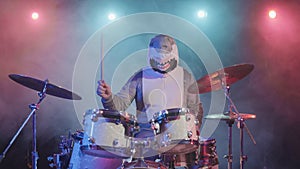 A musician in a festive shark costume plays drums and hits percussion cymbals. A musician plays at a festive concert in