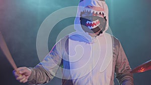 A musician in a festive shark costume plays drums and hits percussion cymbals. A musician plays at a festive concert in