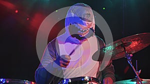 A musician in a festive shark costume plays drums and hits percussion cymbals. A musician plays at a festive concert in