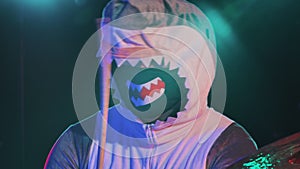 A musician in a festive shark costume plays drums and hits percussion cymbals. A musician plays at a festive concert in