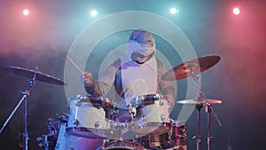 A musician in a festive shark costume plays drums and hits percussion cymbals. A musician plays at a festive concert in