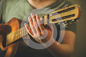 A musician in a green t-shirt plays an old acoustic guitar