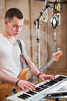 Musician with a guitar around his neck plays keyboard