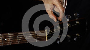 musician guitar player tunes guitar, hand close-up on black background