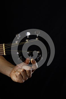 musician guitar player tunes guitar, hand close-up on black background. vertical orientation