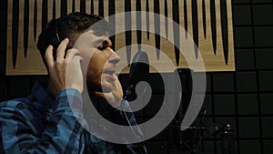 Musician in headphones singing to microphone at recording studio. Professional male singer recording the song at home sound studio