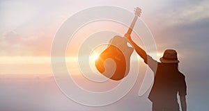 Musician holding acoustic guitar in hand of silhouette on sunset