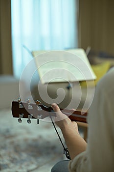 Musician holding acoustic guitar playing music, close-up. Guitarist perform melody with musical sheet. Musical education