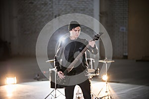 A musician man holding guitar and playing it on the background of a drum-kit