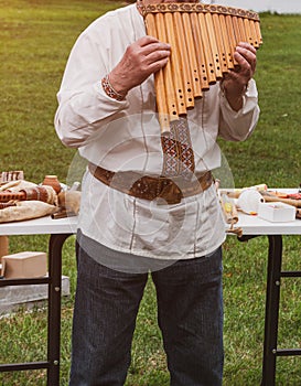 Musician man in vyshyvanka plying sopilka rebro ethnic woodwind musical instrument. Pan flute music festival in Ukraine