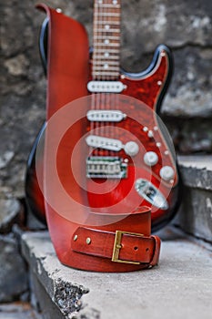 The musician places his red Fender Squier Stratocaster on the steps of the old building. A beautiful strap for a guitar.