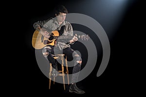 Musician playing acoustic guitar, sitting on high chair, black background with beautiful soft light