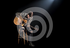 Musician playing acoustic guitar, sitting on high chair, black background with beautiful soft light