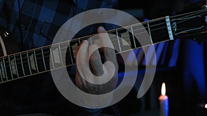 Musician is playing chords on acoustic guitar in dark recording studio with light on background. Male solo guitarist plays lyric m