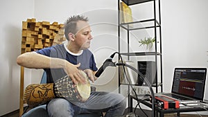 Musician playing djembe drum instrument in home music studio.