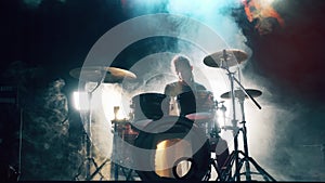 Musician is playing the drum set in the dark clouded studio. Male drummer playing drums in smoke.