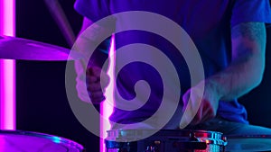 Musician playing drums in the background pink neon tubes. Close up of a man's hand playing on snare and hihat with