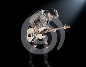 The musician plays bass guitar, on a black background with a beam of light