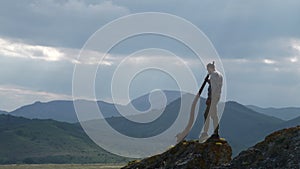 The musician plays the Didgeridoo, an Australian aboriginal musical instrument. A man stands on a ledge of a rock on a