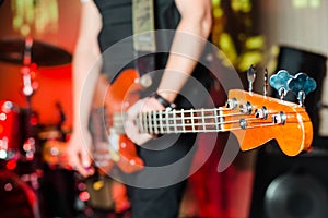 The musician plays the electric bass guitar on stage. Guitar neck close-up on a concert of rock music in the hands of a musician