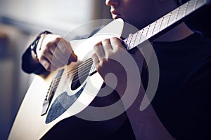 A musician plays his acoustic guitar, holding the fretboard at the base