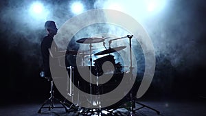 Musician plays professionally good music on drums using sticks. Smoky background. Silhouette. Slow motion