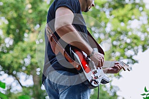 A musician plays a red Fender Squier Stratocaster electric guitar and stands on an old brick wall.