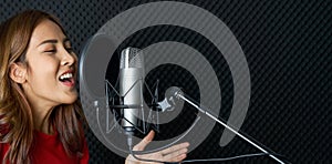 Musician producing music in professional recording studio. Young asian woman in red t-shirt singing in front of black soundproof