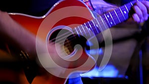 Musician at rock concert - guitarists plays red acoustic guitar in night club, close up
