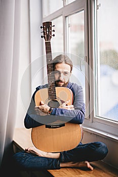 Musician sitting next to a window with a classical guitar