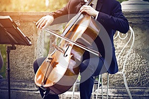 Musician in a suit sitting on a white chair and playing on cello