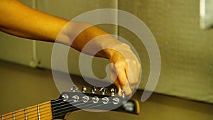 Musician tuning electric guitar. Hand twists guitar pegs. The girl guitarist tunes the tuning pegs