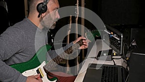 Musician tuning his electric guitar with mixing console at recording studio.