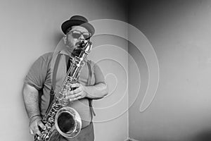 Musician wearing hat, sunglasses, suspenders and with his tenor sax