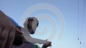 musician wearing sunglasses and cap plays chords on guitar