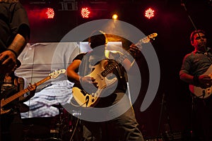 Musicians generating music by playing guitars, bass, drums, vocalizing in Mexico city with red an yellow lighting