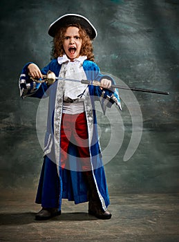 Musketeer. Little emotional girl, child with curly hair like little prince posing over dark vintage background. Concept